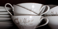 Several old china coffee cups, plates, and saucers stacked within a cupboard.